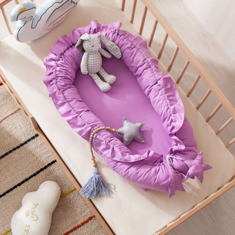 Purple baby nest with toys inside, placed on a wooden crib in a nursery setting.