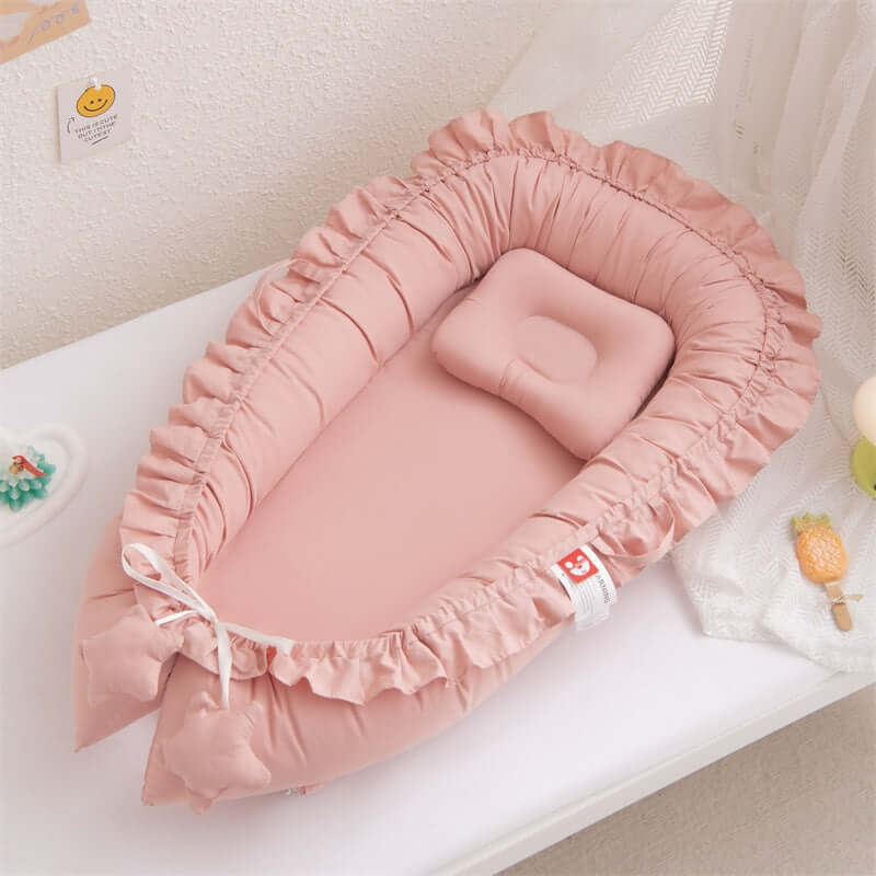 Pink baby crib with ruffled edges on a white surface